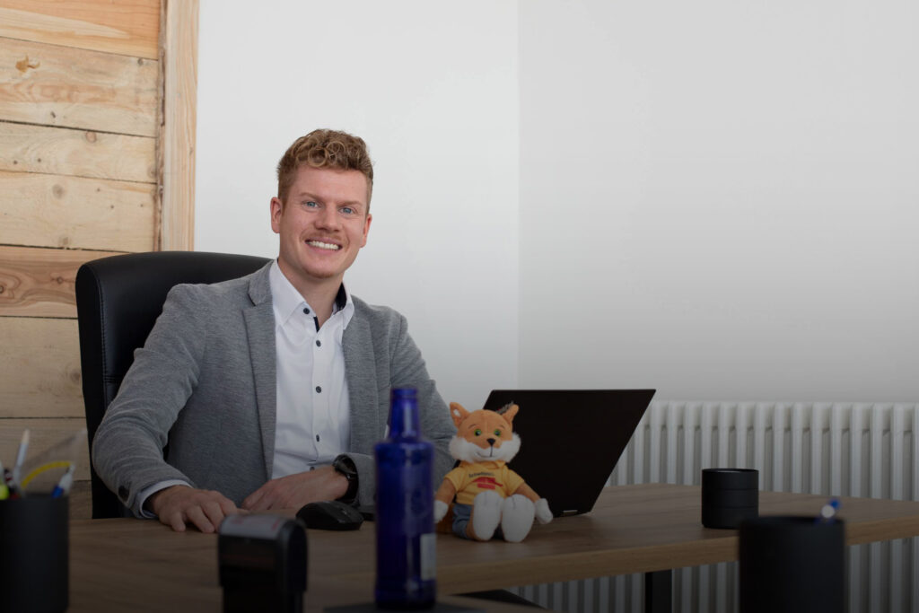 Hintergrundbild Steffen Martens am Schreibtisch mit einem Laptop und dem Schwäbisch Hall-Fuchs