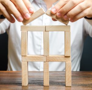 Ein Mann baut mit Dominosteinen ein kleines Haus auf einem Tisch