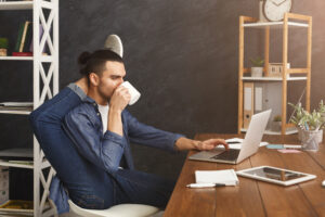 Kurze Pause für Yoga im Büro. Flexibler Mann, der am Arbeitsplatz Yoga praktiziert, während er auf dem Laptop tippt und Kaffee trinkt, Platz zum Kopieren. Aktiver Mitarbeiter bei der Arbeit, gesundes Lebensstilkonzept