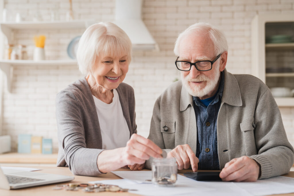 Zwei Großeltern legen Münzen in Sparbüchse, sie Sparen für Notgroschen, Rente, Hypothekendarlehen zu Hause und für ihre Enkelkinder