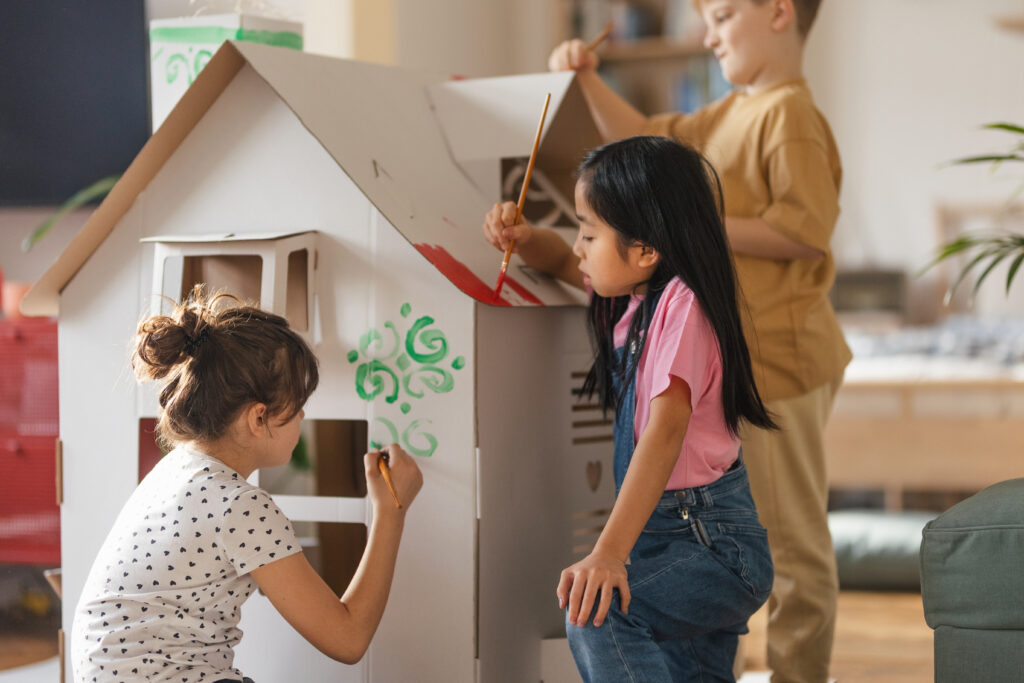 Glückliche Kinder bemalen gemeinsam ein handgefertigtes Papphaus.