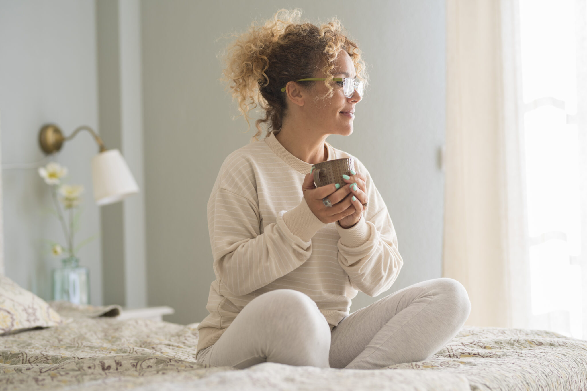 Eine zufriedene Frau mit einem Becher in der Hand, die auf einem Bett sitzt