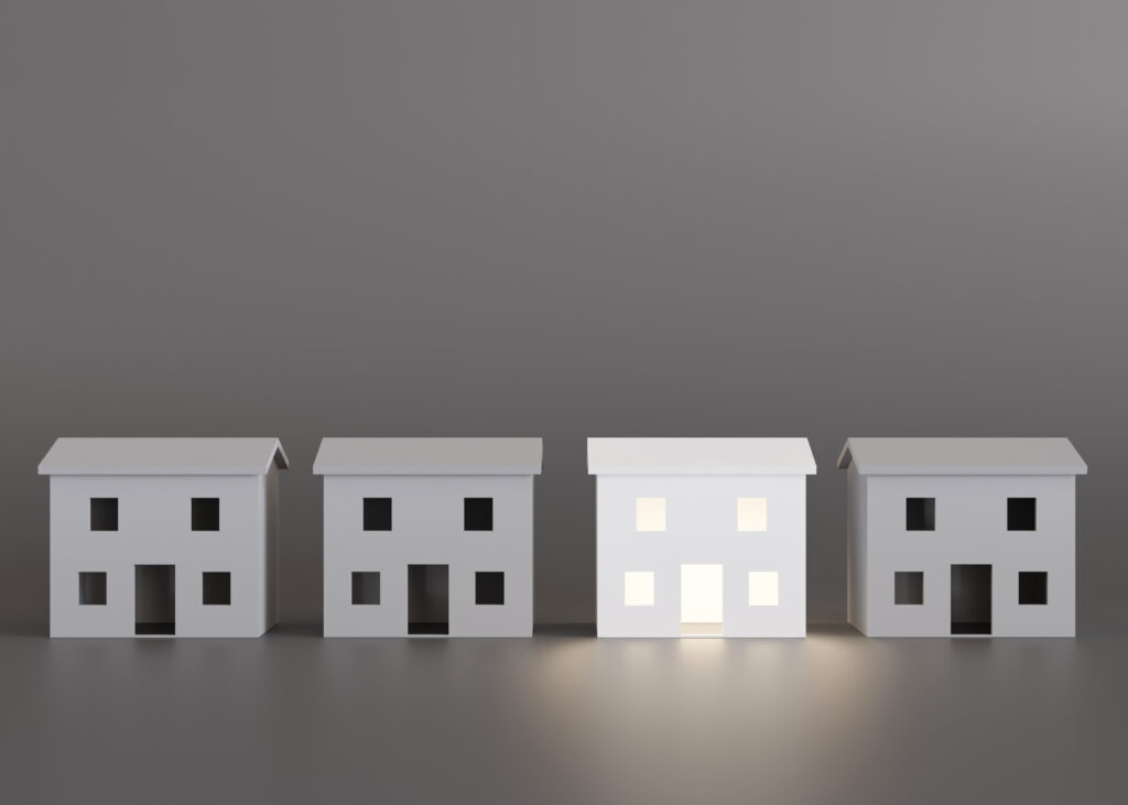 Vier gleiche weiße Modelle von einem Haus und das dritte Haus ist im Gegensatz zu den anderen beleuchtet.