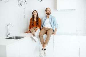 Ein Junges Paar genießt die neue Wohnung und sitzt gemeinsam in der weißen, modernen Küche und ist glücklich